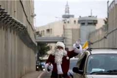 A Palestinian dressed as Santa Claus gestures as the Latin Patriarch of Jerusalem Pierbattista Pizzaballa arrives through an Israeli checkpoint to attend Christmas celebrations, in the West Bank city of Bethlehem December 24, 2016. REUTERS/Mussa Qawasma - RTX2WDH7