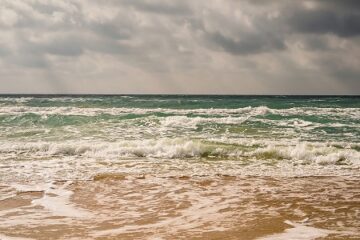 Storm on the sandy beach of the Black Sea coast, emerald clear water, warm day. The sun's rays make their way through the clouds in the sky.