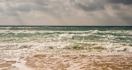 Storm on the sandy beach of the Black Sea coast, emerald clear water, warm day. The sun's rays make their way through the clouds in the sky.